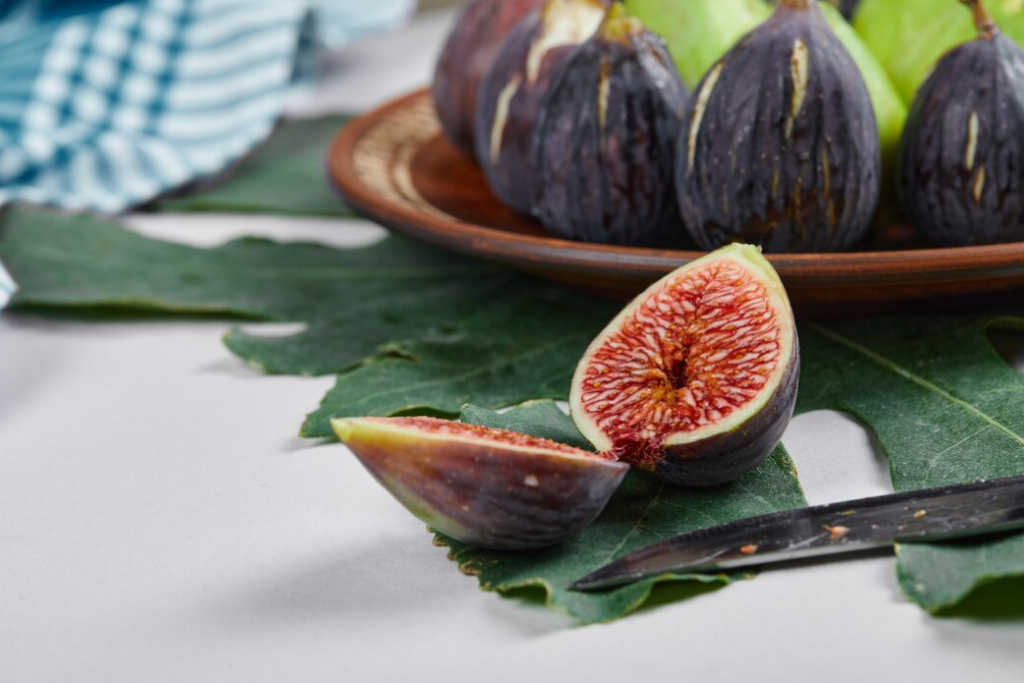 purple figs on the plate, one fig on the leaf on the white table 